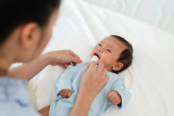 mother using finger to clean newborn baby mouth (tongue and gum) with clean gauze on bed