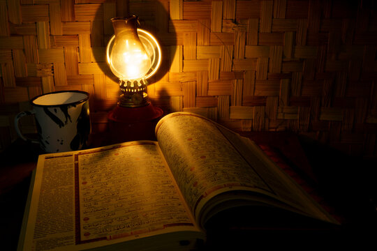 Holy Quran on the wooden table with vintage traditional kerosene lamp and woven bamboo as background.