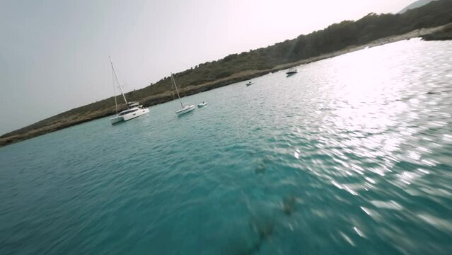 FPV drone flight over the sea alongside the spectacular cliffs with sialboats docked seaside in Cala Varques, Mallorca, Spain.