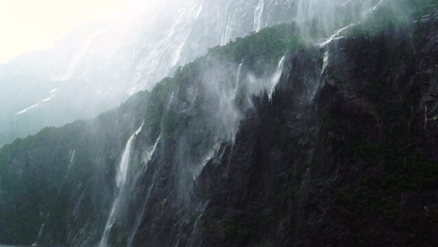 Fantasy waterfalls on rocks of Milford Sound, New Zealand on heavy rain blown by wind