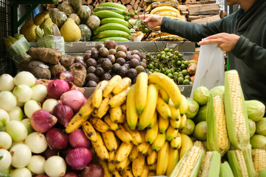 Unrecognizable man buying tropical fruits, melicoccus bijugatus, in a vegetable market.