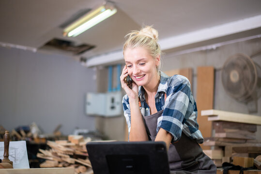 Young carpenter women using mobile phone and working in wood workshop