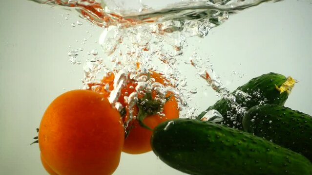 Falling of cucumbers and tomatoes in water. Slow motion.