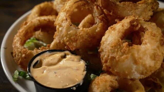 Golden fried huge Onion rings piled high with sauce on the side, slider close up 4K
