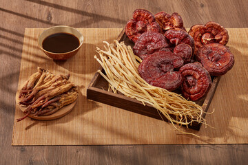 Dangshen and lingzhi mushroom placed on a square wooden tray with a dish of Red ginseng and a bowl of medicine. For medicine advertising, photography traditional medicine content