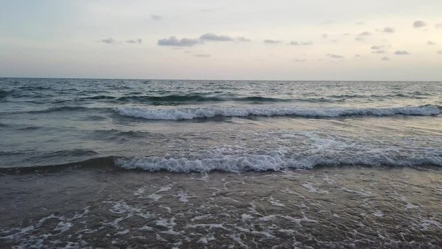 Waves gently wash up onto the beach and recede as the sun is setting.