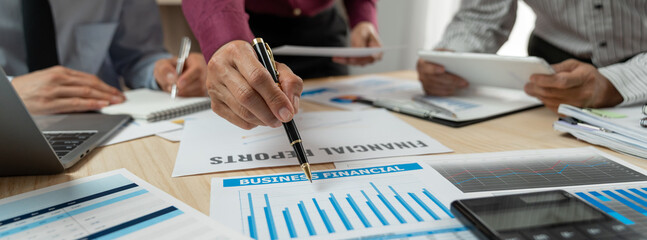 A group of Asian businessmen are brainstorming to analyze financial reporting situations. Calculate investments, income, taxes, accounts from data reference graphs. Income from laptop at office desk.