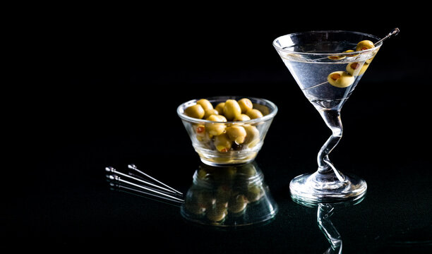 Vodka martini with a cocktail pick of olives and a bowl of olives beside.