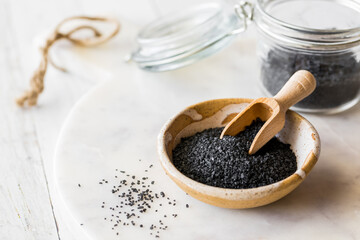Black Hawaiian rock salt in a bowl with a small wooden scoop.