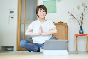 タブレットPCの画面を見ながら部屋でストレッチする女性