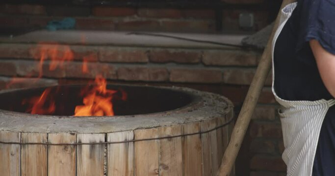 Female Baker Standing By Traditional Clay Oven (Tone) With Fire In Sighnaghi, Georgia. medium shot