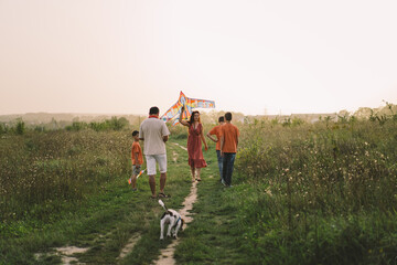 Happy family and children run on meadow with a kite in the summer on the nature. Family playing with kite while running along rural summer field. Family day