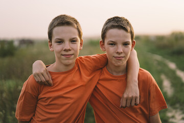 Funny twin brother boys in orange t-shirt playing outdoors on field at sunset. Happy children, lifestyle. - obrazy, fototapety, plakaty