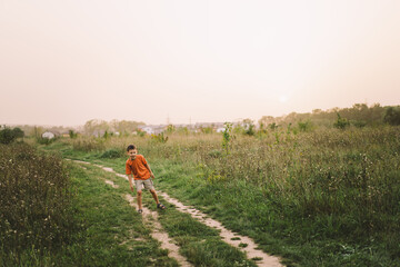 Portrait of a funny boy in a orange T-shirt and playing outdoors on the field at sunset. Happy child, lifestyle.