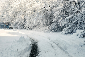 A winter highway with snow mounds, snow-covered pines and a mountain under a blue sky. A snow-covered road under a blue sky. A snow-covered road near a frozen forest. 