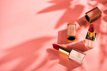 Red lipstick beauty product on a pink background. Sun shadows from flowers, copy space - obrazy, fototapety, plakaty