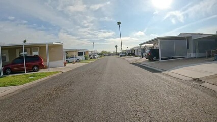 Point of view - driving past trailer homes and a man on a golf chart in a gated community and RV Resort for seniors and winter Texans in the Rio Grand Valley of Texas
