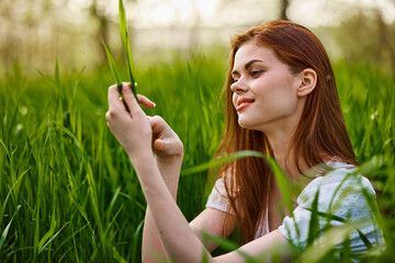 portrait of a blissfully smiling woman sitting in the grass with a leaf in her hand