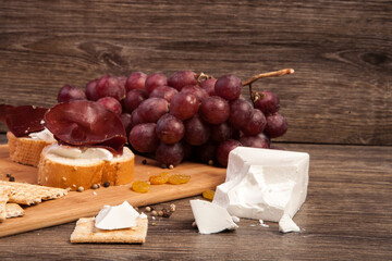 Ham, crackers, grape and white cheese on wooden background in studio photo