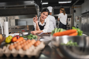 Happy Asia woman assistant chef cooking with raw material food at kitchen background