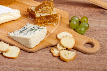 Honey, white cheese and other cheese with grape on wooden background. Delicatessen food