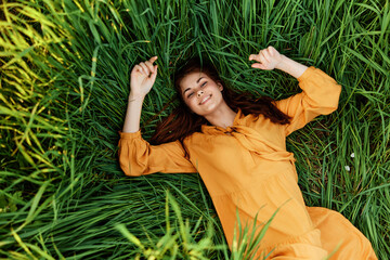 a joyful woman in a long orange dress lies in the tall green grass and looking at the camera smiles broadly