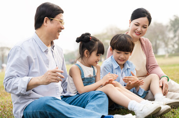 Fototapeta premium image of an asian family sitting together on the grass at the park