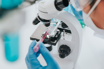 Scientist or doctor wear medical protective mask looking at blood samples under microscope.