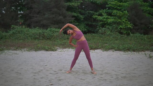 Young fit woman out for her morning routine, side-bend stretch, on a pristine beach.
