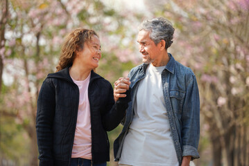 portrait romantic asian senior couple enjoy walking,talking in nature and seeing the flowers on...