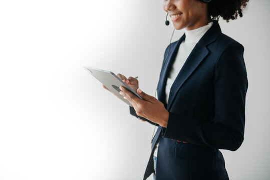 Serious call center operator in wireless headset talking with customer, woman in headphones with microphone consulting client on phone in customer support service in business center.
