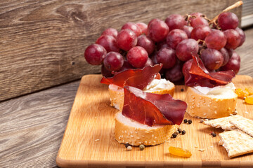 Ham, white cheese and grape on wooden background in studio photo