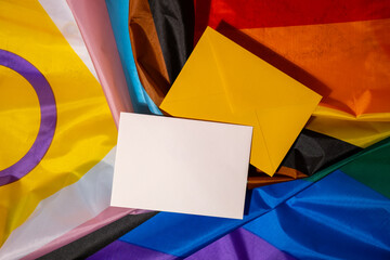 Empty paper blank on Rainbow LGBTQIA flag made from silk material. Mock up template copy space for...