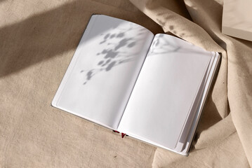 Open notepad blank sheets and floral sunlight shadows on neutral beige linen background, mock up...