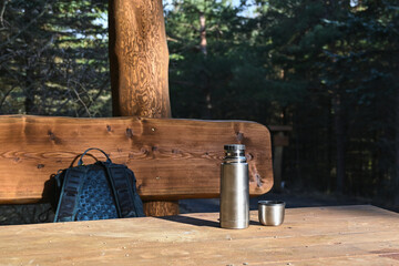 Wooden table and bench with tourist thermos and backpack under the tourist shelter