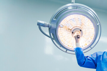 Doctor or surgeon in blue gown holding surgical lamp to adjust light inside operating theatre with...