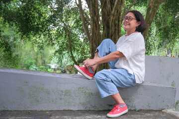 Asian woman sitting alone in the park, fixing her shoe lace, after a long walk