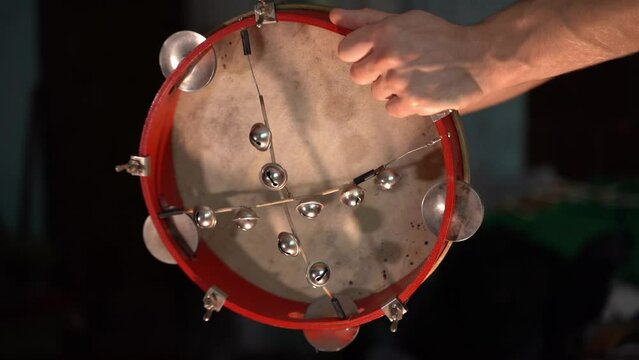 The hand beats the membrane of a tambourine close-up in the dark