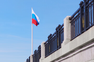 The flag of Russia rises above the embankment. Selective focus on the flag of the Russian Federation. Fencing in blur