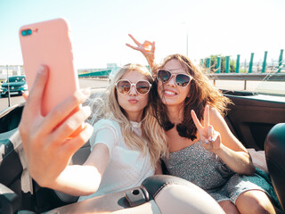 Two young beautiful and smiling hipster female in convertible car. Sexy carefree women driving...