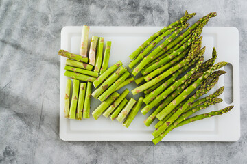 Fresh raw green asparagus on a white cutting board close-up on the kitchen table, flat lay, copy space