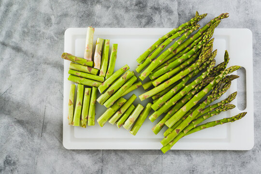 Fresh raw green asparagus on a white cutting board close-up on the kitchen table, flat lay, copy space