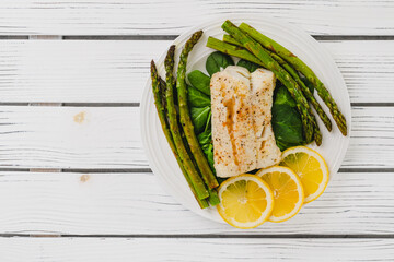 Cod fillet baked with garlic butter sauce served with fresh spinach and roasted asparagus on a...