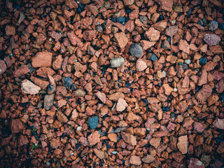 Ground texture with small multi-colored stones. Pebbles of red and terracotta color. Stone decoration of sidewalks and footpaths in parks, squares and courtyards. Perfect for background and design.