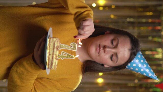 Beautiful happy young woman wearing sweater holding birthday cake number 74 golden candles burning by lighter. Concept of celebrating birthday and anniversary. POV.