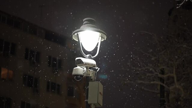 Slow motion snow fall over street light ontop of safety and security camera pole