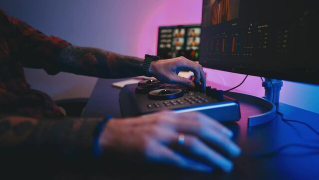 Close-up of a man's hand making edits on a special panel. Young man in glasses working on video editing on computer doing montage and color correction. Concept of creating video content.
