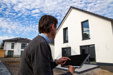 Symbolbild Architekt bzw. Bauherr: Mann mit Laptop vor einem Einfamilienhaus (model released)