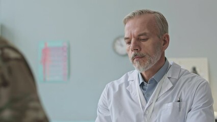 Tilt up of Caucasian mid aged military doctor taking notes in medical document while listening to soldier speaking about his health during appointment at hospital - Powered by Adobe