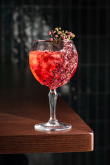 delicious light red cocktail in Tall glass of gin tonic filled with ice and Red flowers for decoration, dark background, vertical, side view